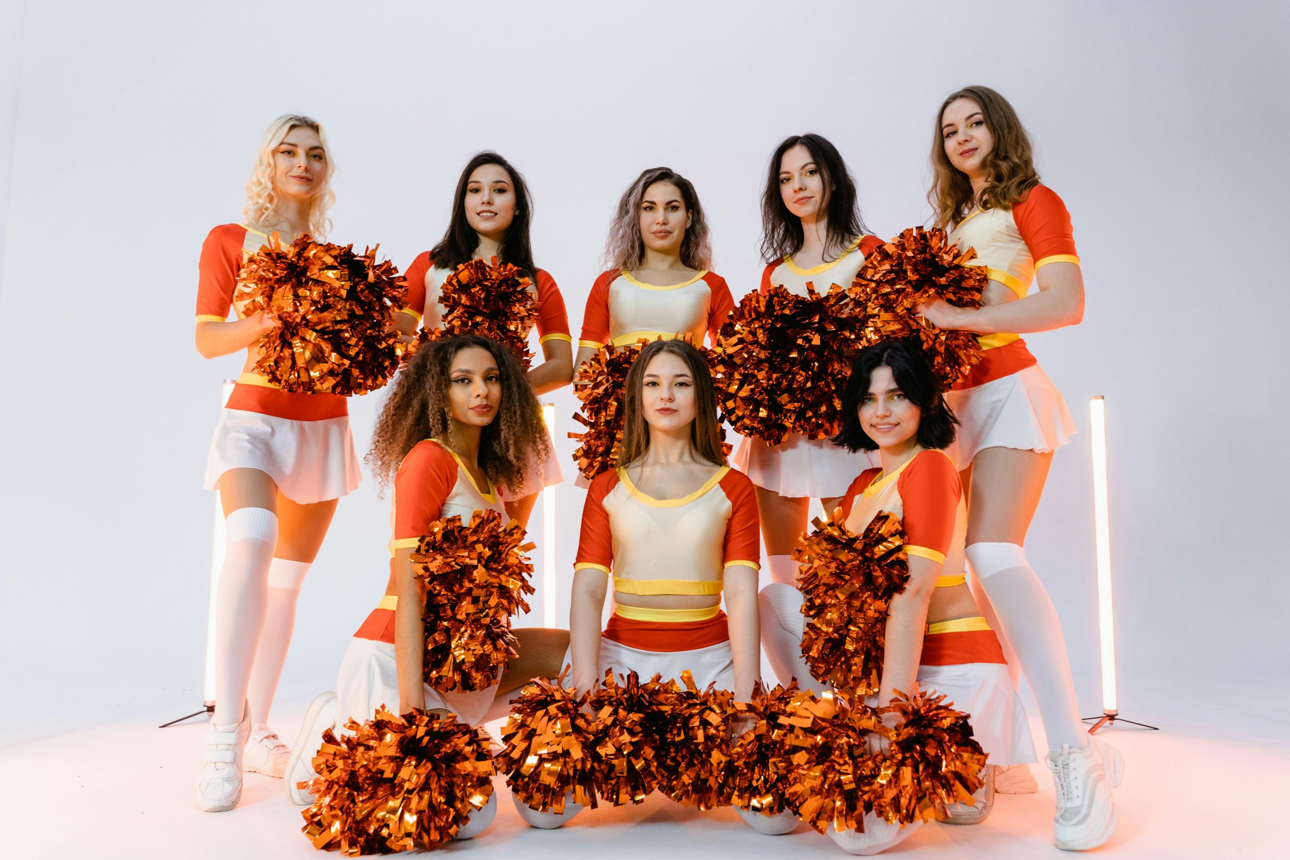Group of diverse cheerleaders in vibrant uniforms posing with pompoms in a studio setting.